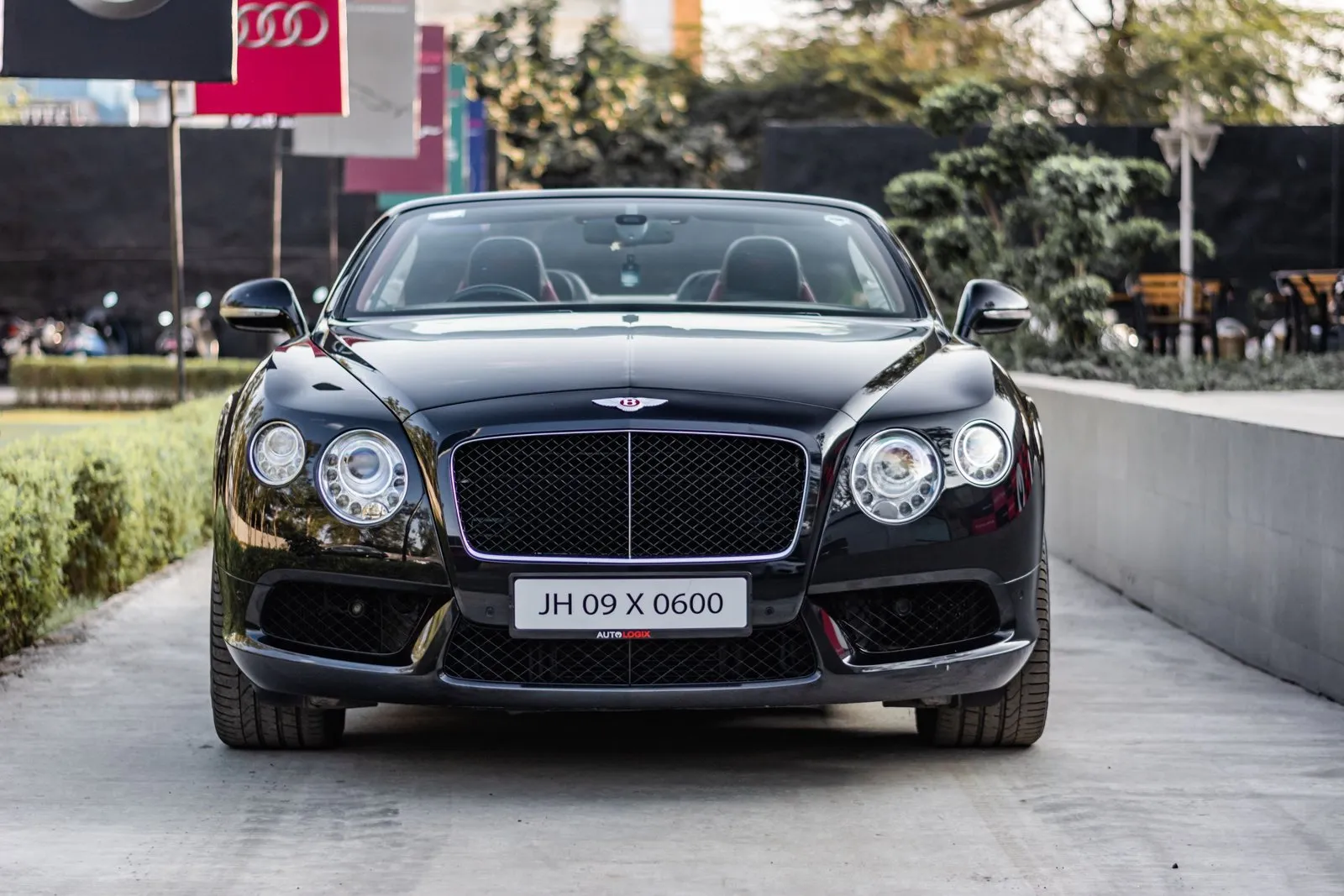 Une Bentley Continental GT noire sur une route côtière au coucher du soleil, reflets brillants.