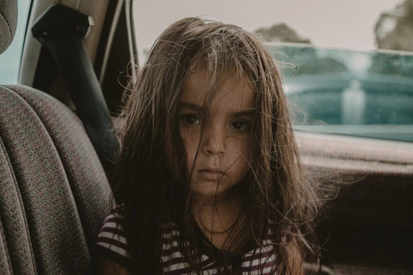 Un enfant souriant installé sur un rehausseur auto, ceinture bien placée sur l'épaule et la hanche.